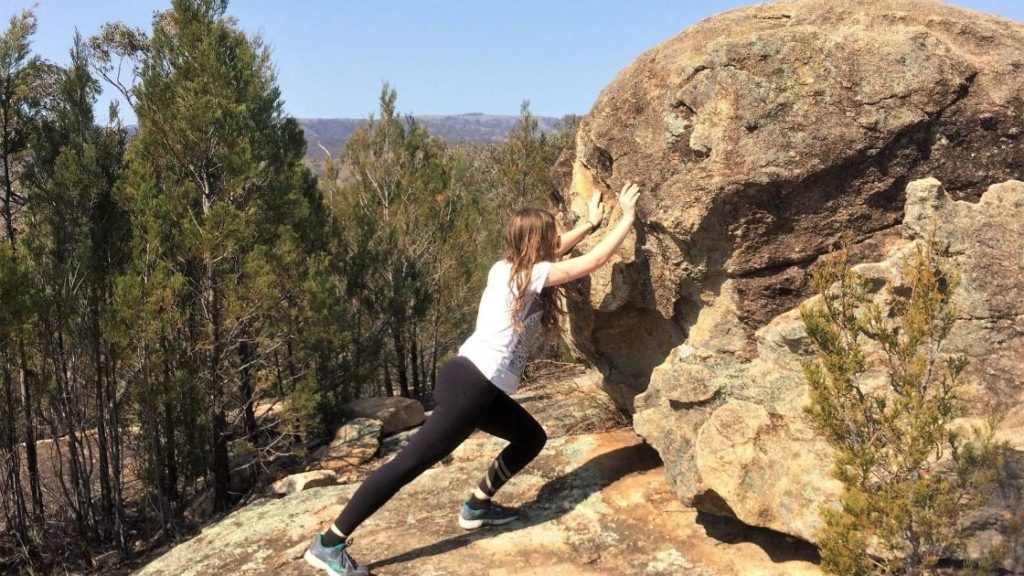 woman pushing against large boulder